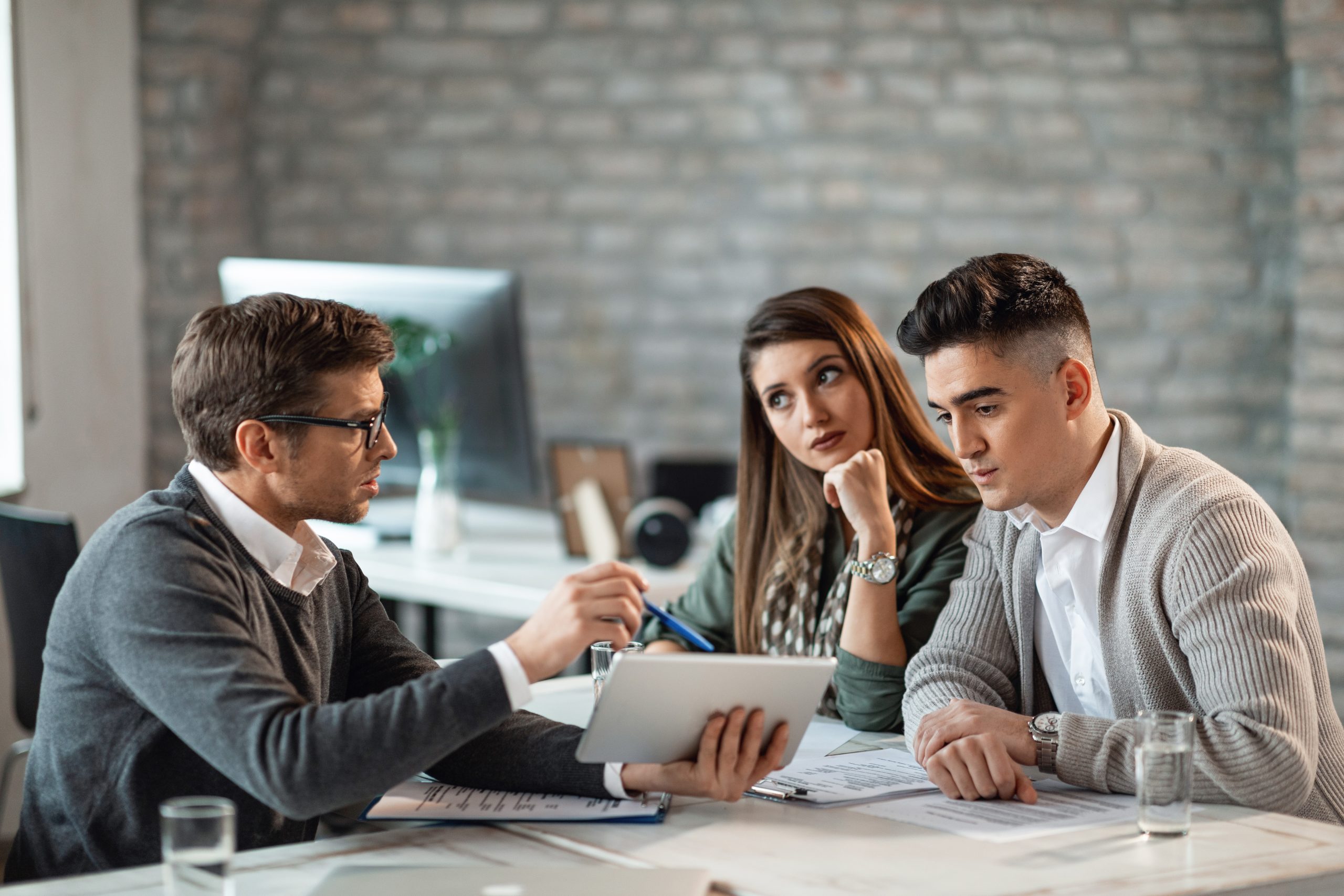pareja joven usando tableta digital con su agente de seguros durante las consultas en la oficina scaled